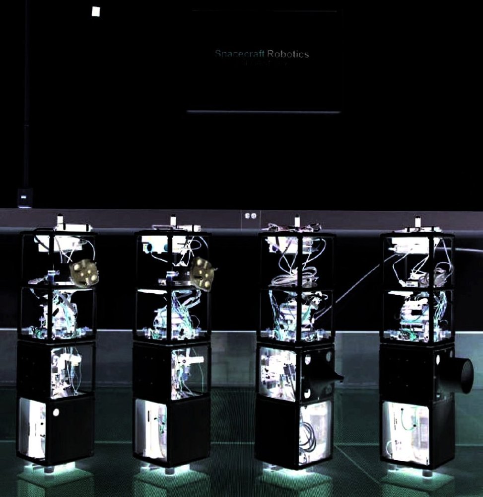 Four dark cube-stack robots glowing from within, afloat on a granite table in a darkened lab