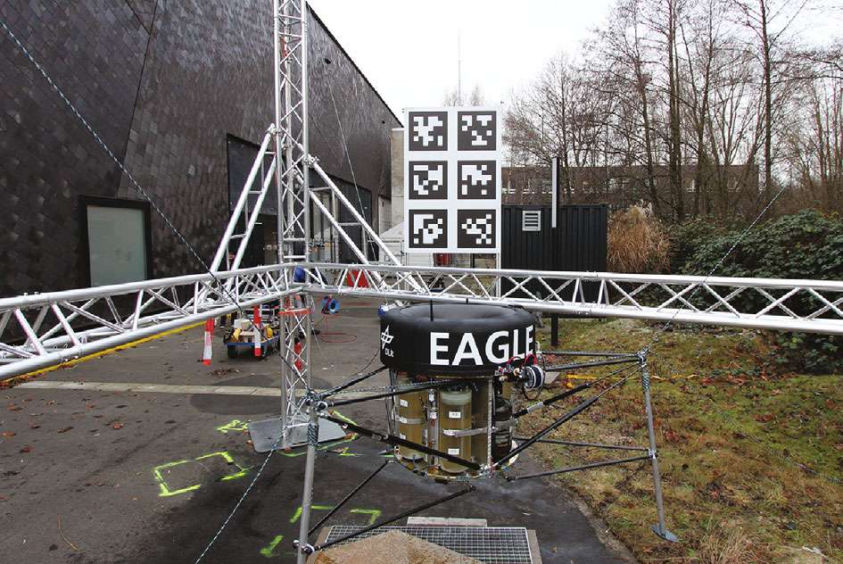 Squat black-topped vehicle lettered EAGLE above olive tanks, legs splayed on a paved yard