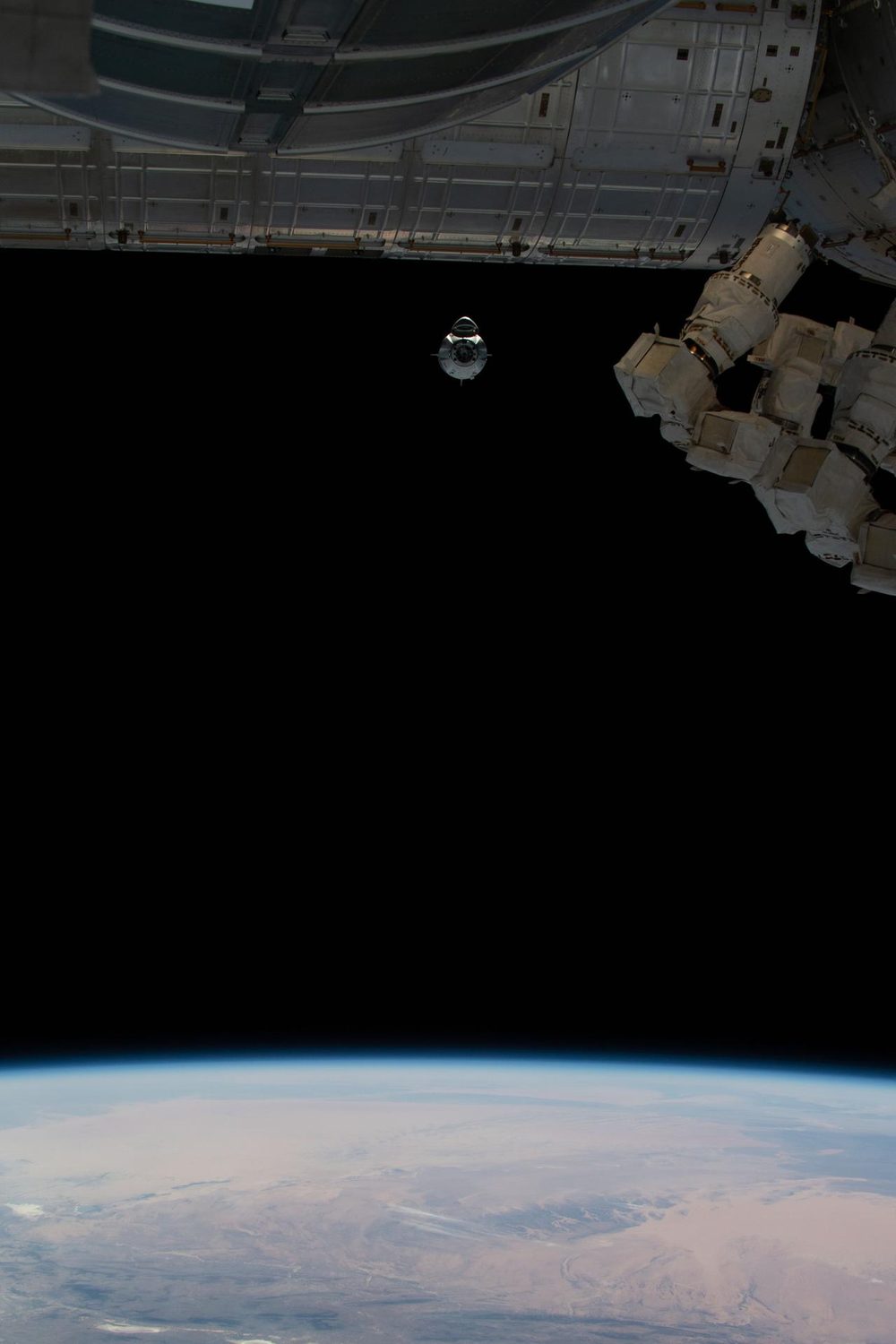 A small bright capsule alone in a wide black gap, station hardware framing the top