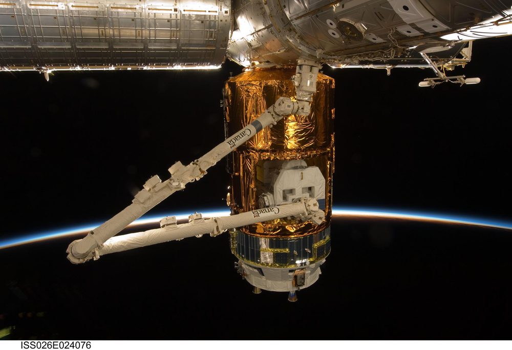 Gold foil cargo cylinder gripped by a white robotic arm beneath a station module