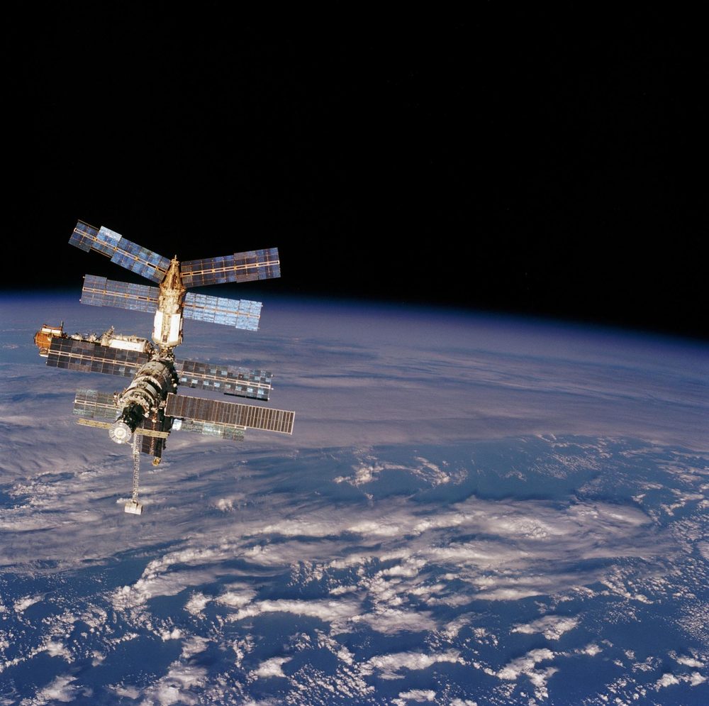 Modules radiating in several directions with solar arrays at many angles, blue Earth beneath