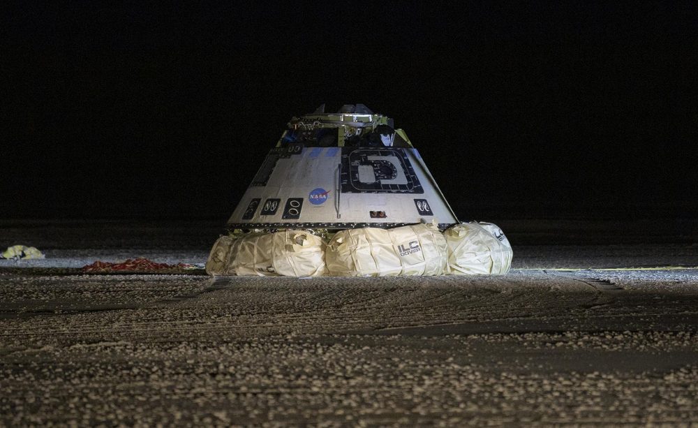 Floodlit conical capsule sitting on inflated airbags on dark desert ground at night