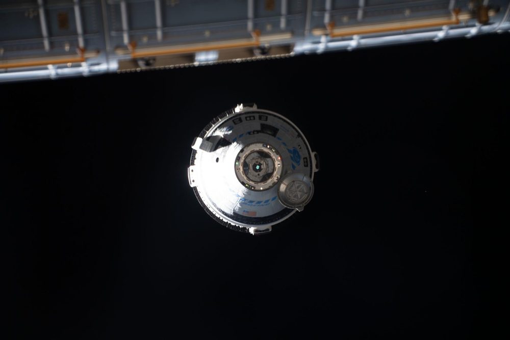 Small sunlit capsule against black, a station radiator panel across the top of the frame