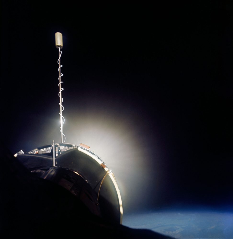 Dark rounded hull with a slender boom above it, a diffuse halo of light behind