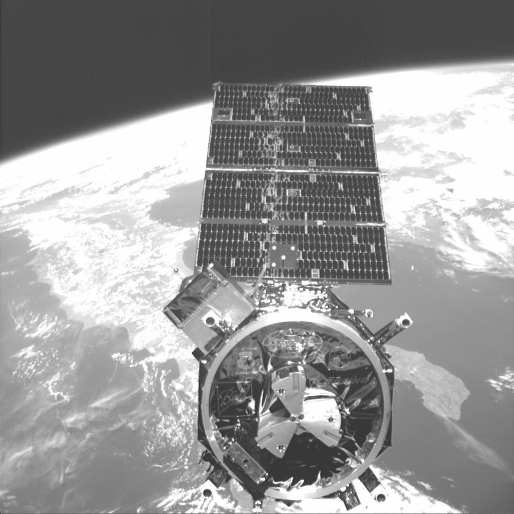 Monochrome view of a small satellite, large circular docking ring facing the camera, Earth behind