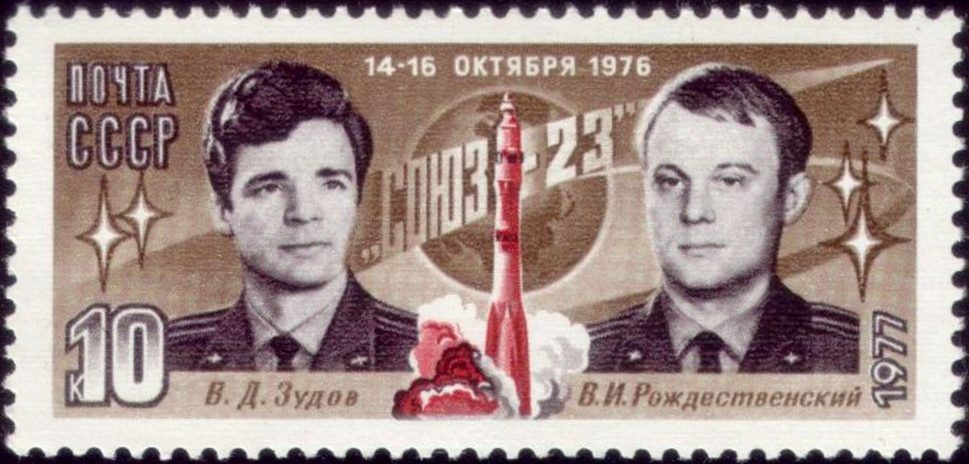 Sepia stamp, two men in dress uniform flanking a red rocket lifting off