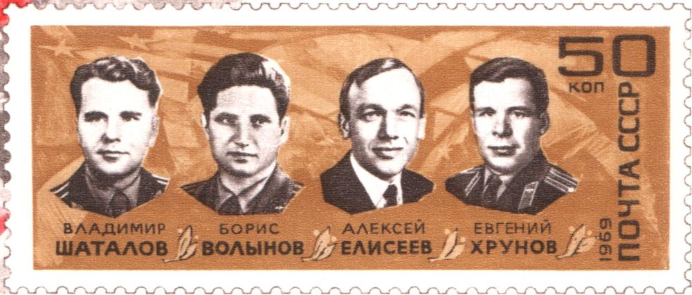 Four monochrome portrait heads in a row on an orange-brown stamp, names lettered beneath