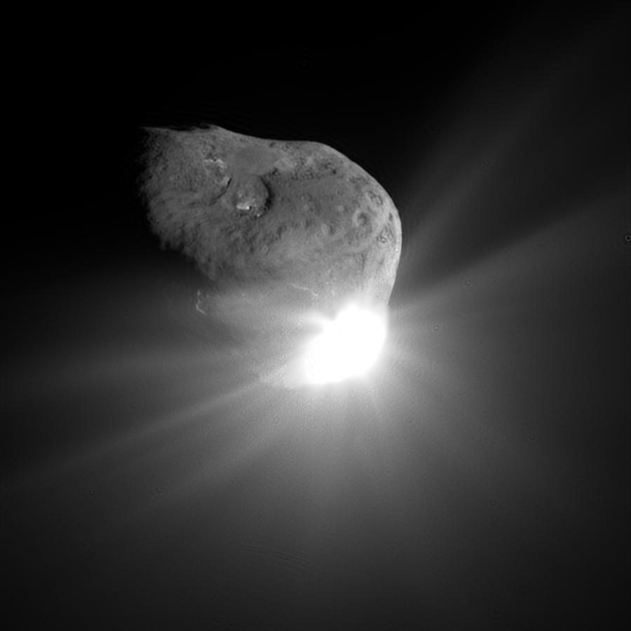 Cratered nucleus above a brilliant white flare, rays of debris spreading outward