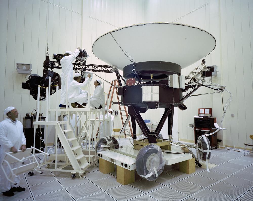 Technicians in white coveralls on a gantry beside a spacecraft with a large dish