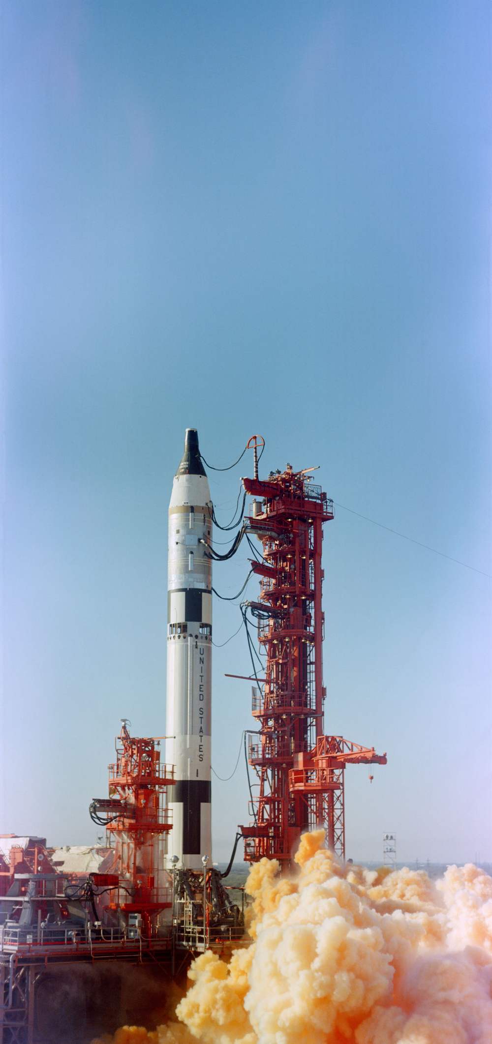 A rocket at the instant of lift-off beside a red service tower, exhaust boiling below