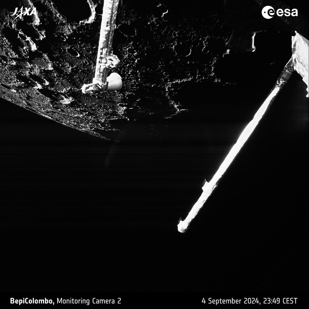 Monochrome frame: cratered ground at top left, lit spacecraft booms crossing the dark