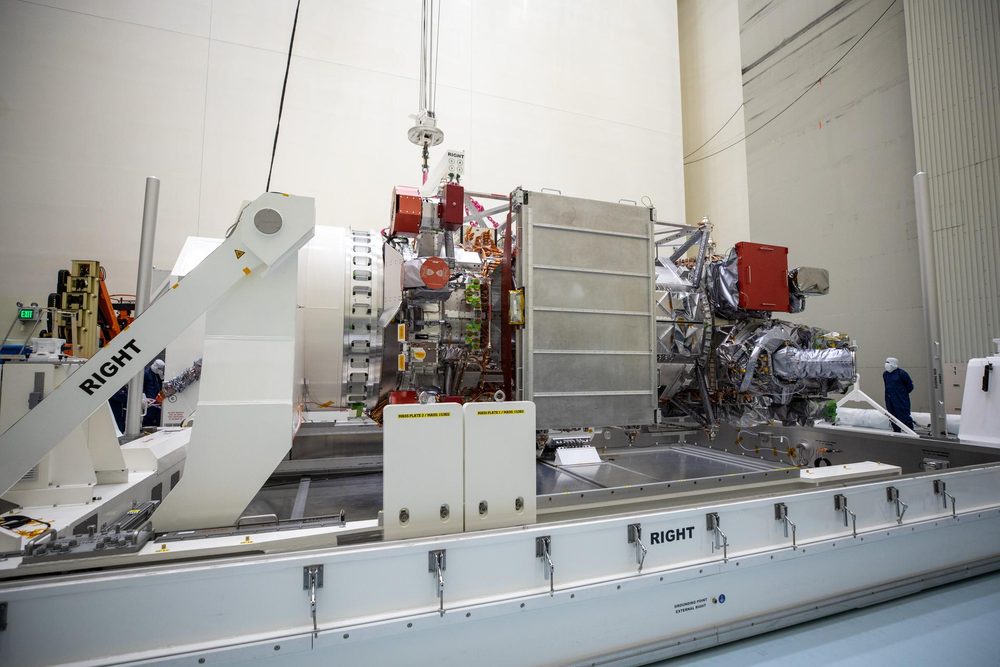 Boxy spacecraft in foil and white panels lying horizontally on a cleanroom cradle