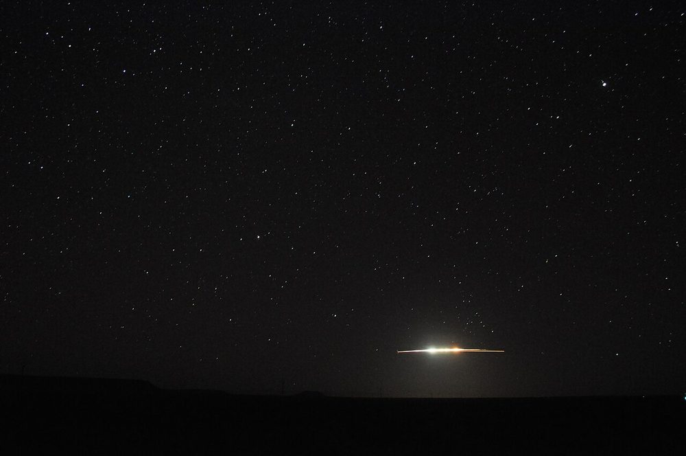 Star-filled night sky above a dark horizon, one bright streak low in the frame