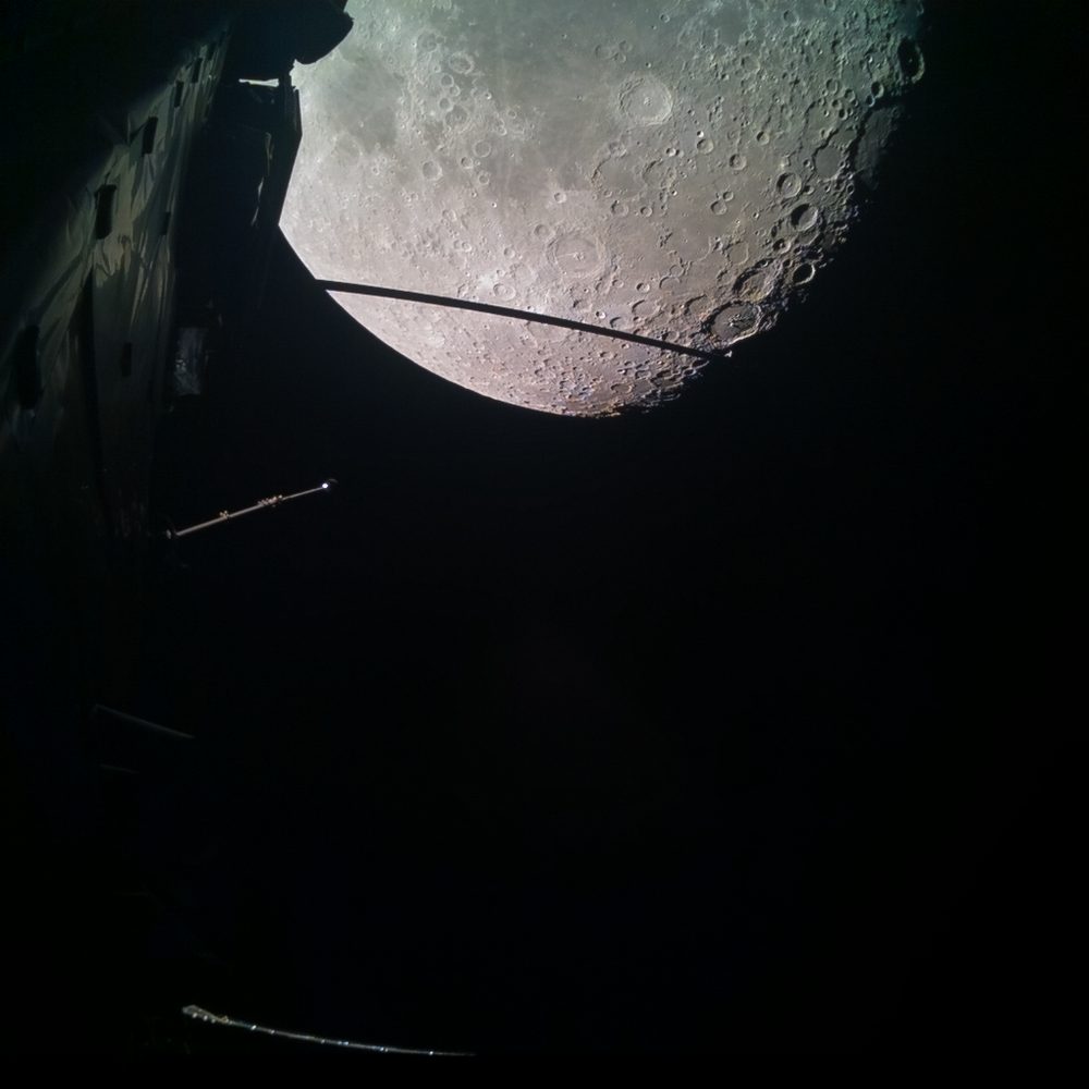 Cratered lunar limb at the top, dark spacecraft structure and a lit boom below