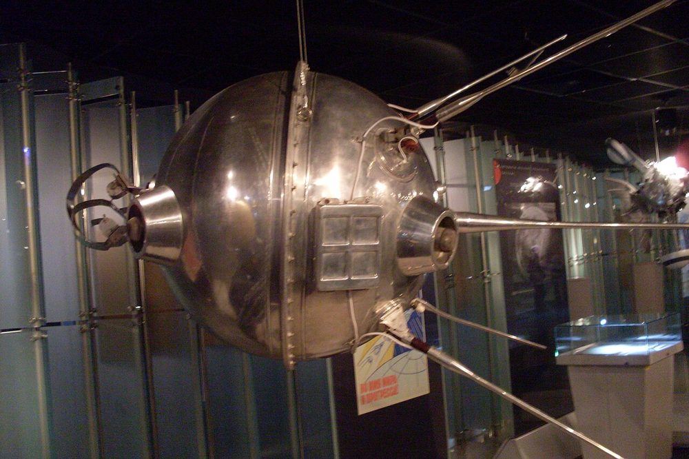 Riveted metal ball with cone-shaped fittings and thin rods, hung in a dim gallery