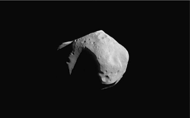 Grey angular body half lost in shadow, a huge crater biting into its edge