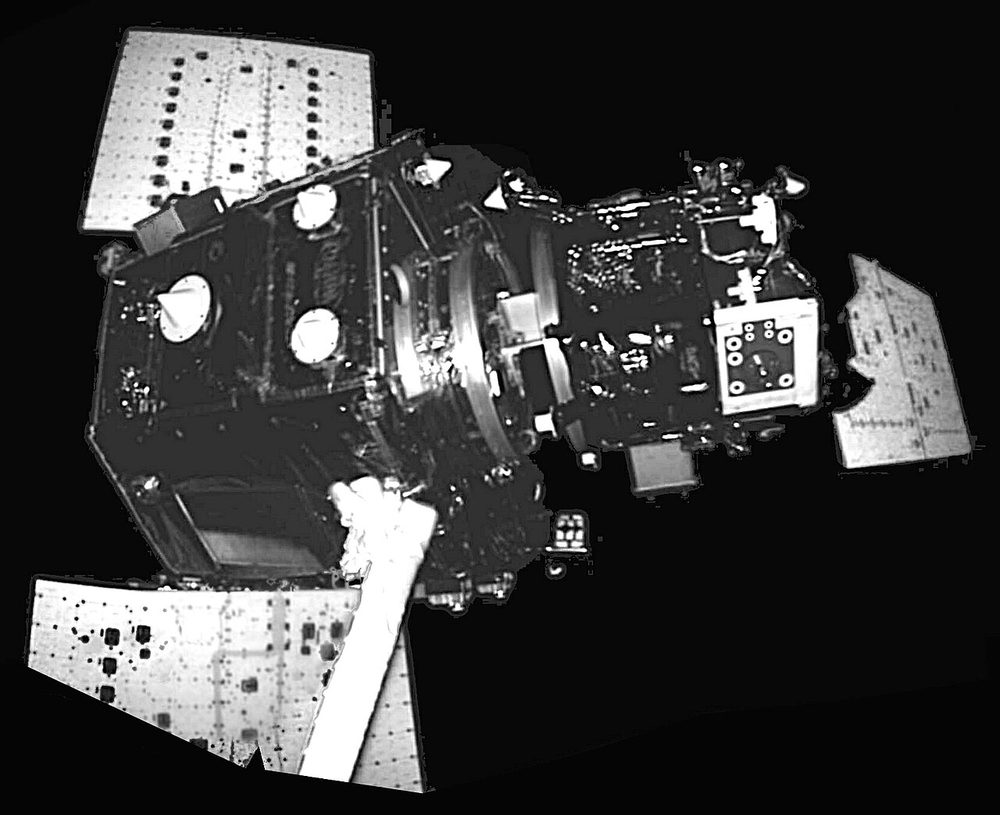 Harshly lit monochrome view of a boxy spacecraft with flat solar panels angled outwards