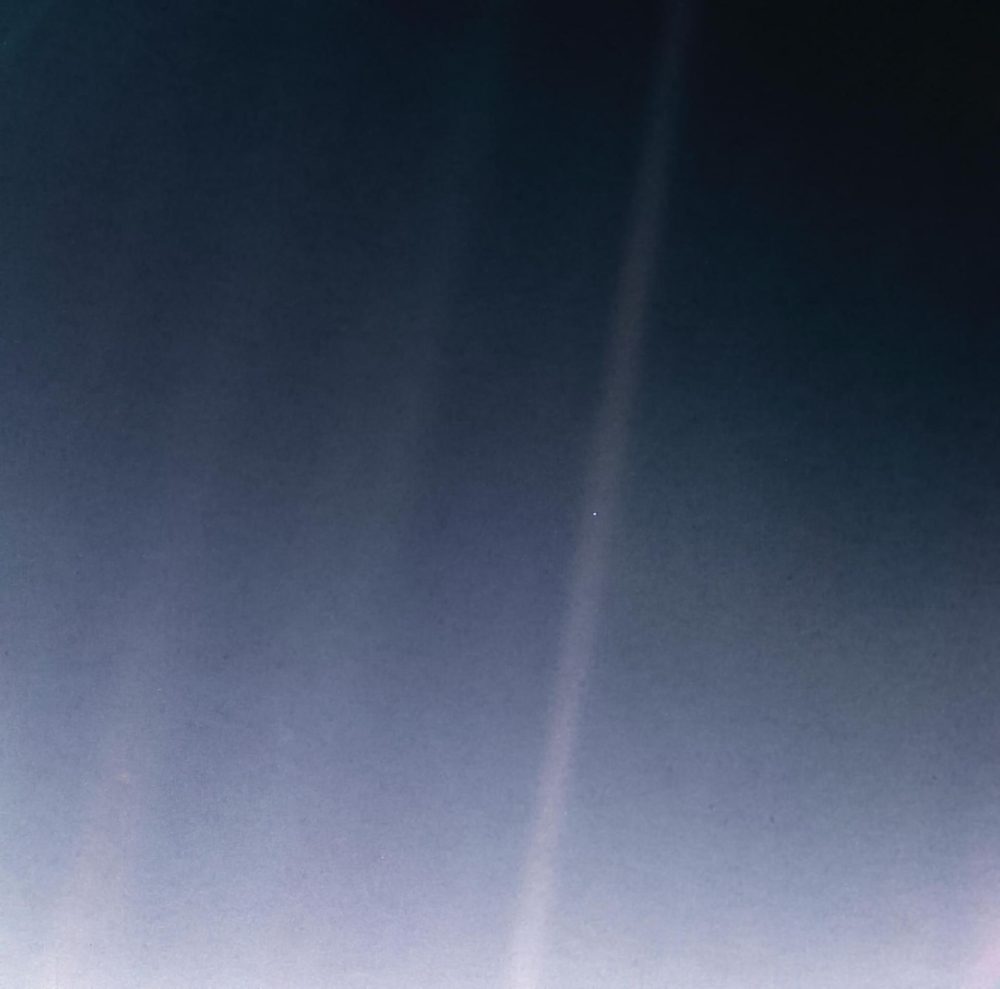 Grainy dark frame crossed by pale bands of scattered light, one tiny speck within a band