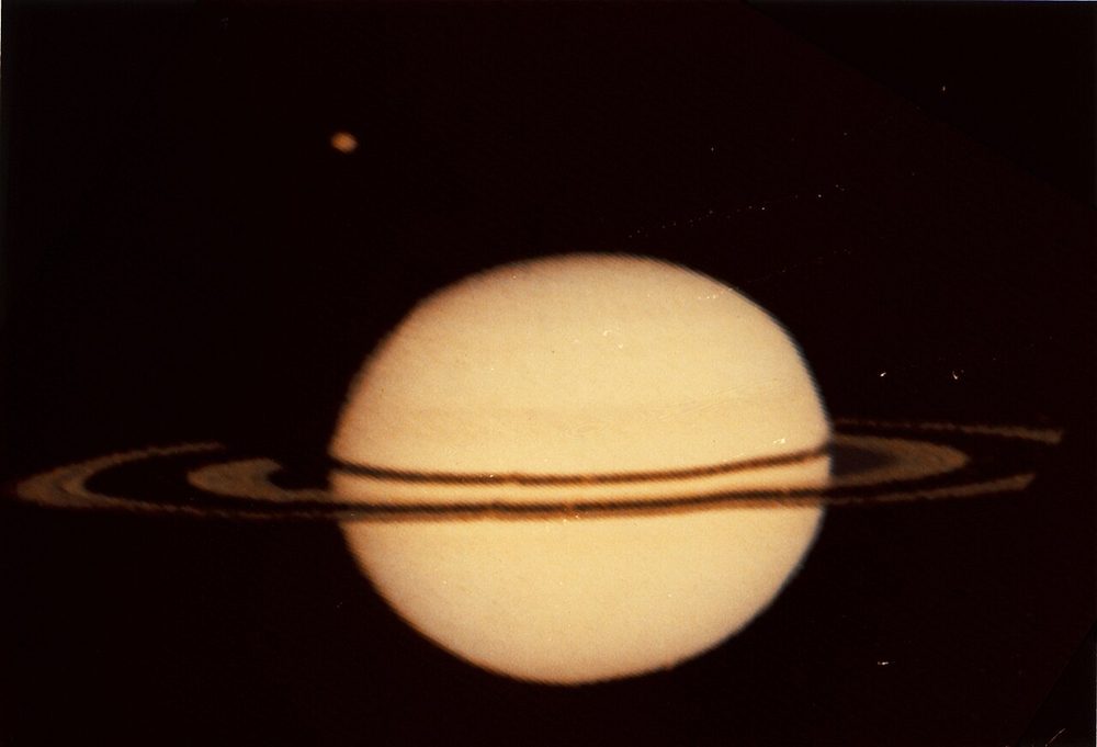 Soft pale disc crossed by thin dark rings, one small point of light above left