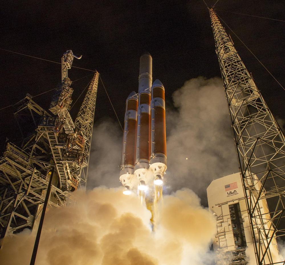 Three-core rocket climbing at night between gantry towers in billowing white smoke