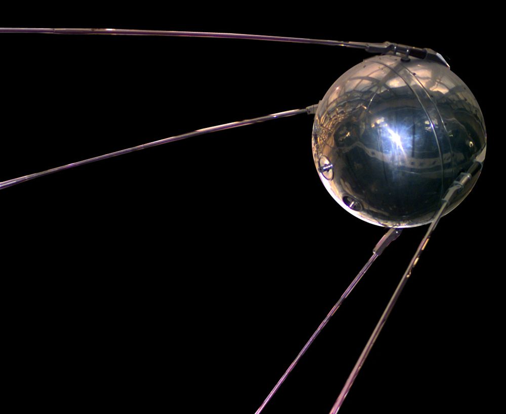 Polished metal sphere trailing four long swept-back whip antennas against black
