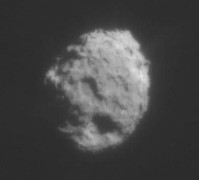 Grainy round body pocked with broad flat-floored depressions, one edge in shadow