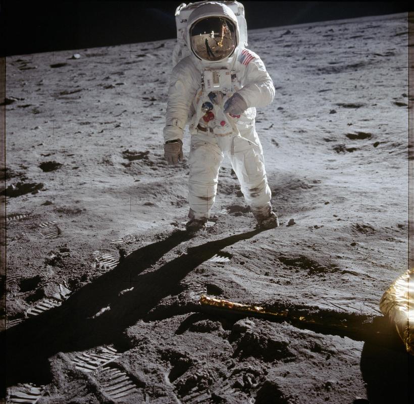 Astronaut in a white suit on grey dust, the lander reflected in his gold visor