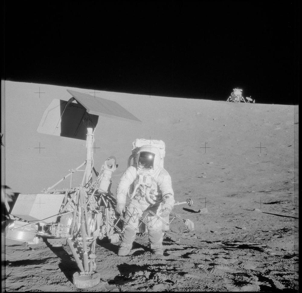 Black and white view up a crater slope, a suited figure standing beside spindly hardware