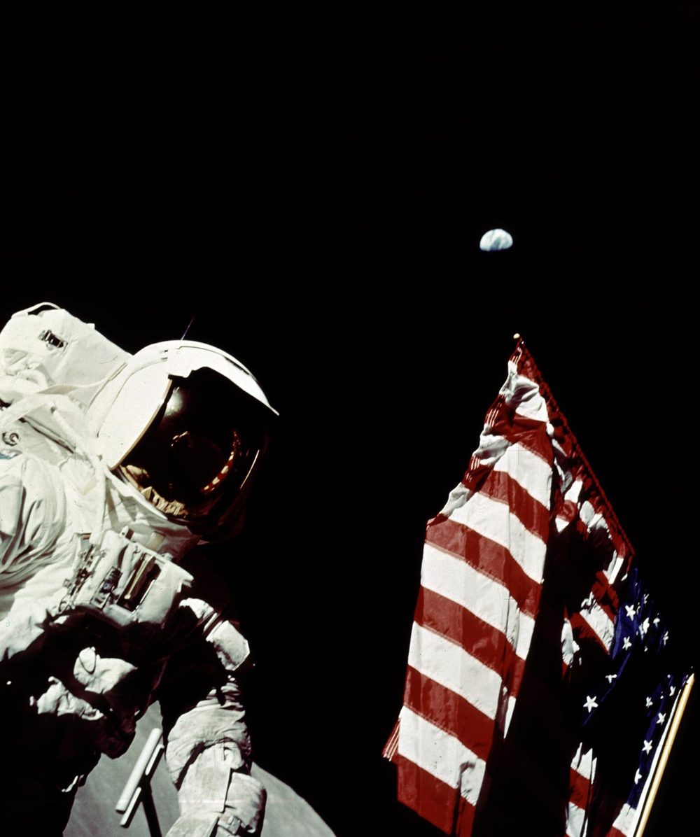 Suited figure beside a Stars and Stripes, a small blue disc high in black sky