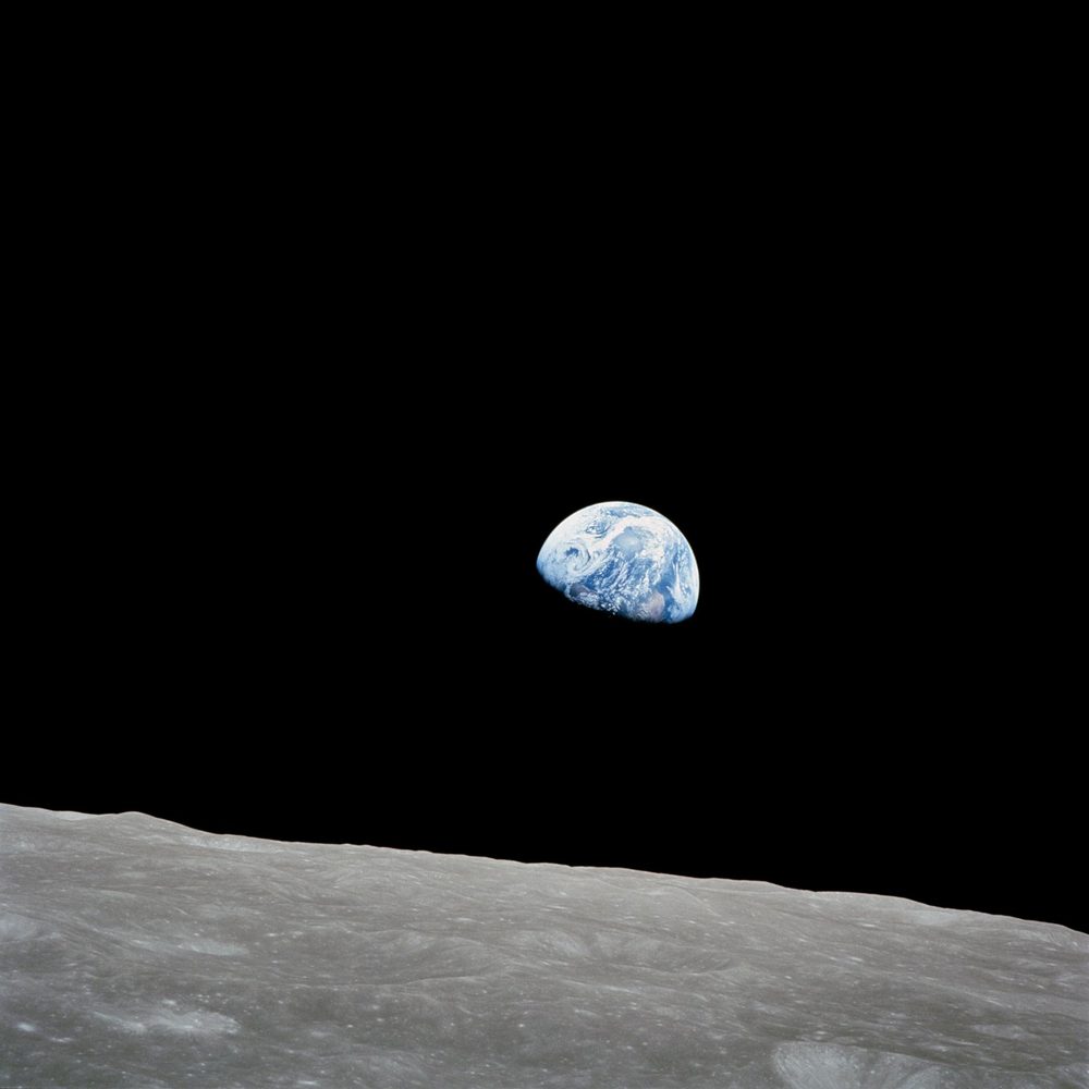 Blue and white Earth, half in shadow, above a grey cratered horizon in black sky