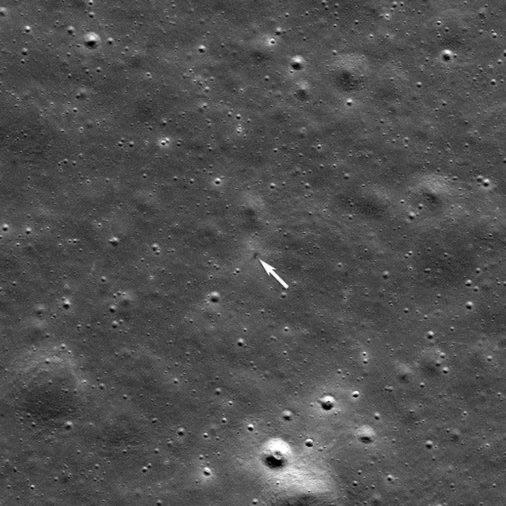 Densely cratered grey plain with a white arrow indicating a faint dark mark