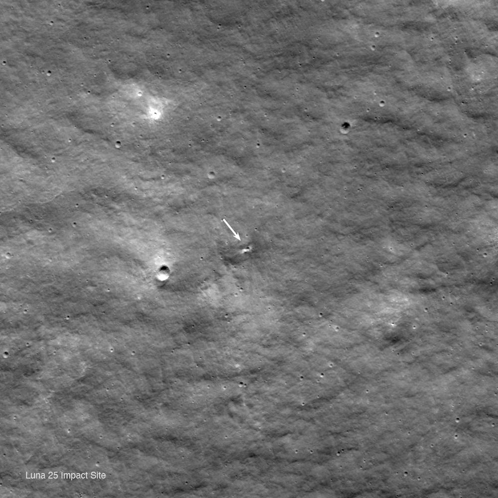 Grey lunar surface with a white arrow pointing at a small dark pit