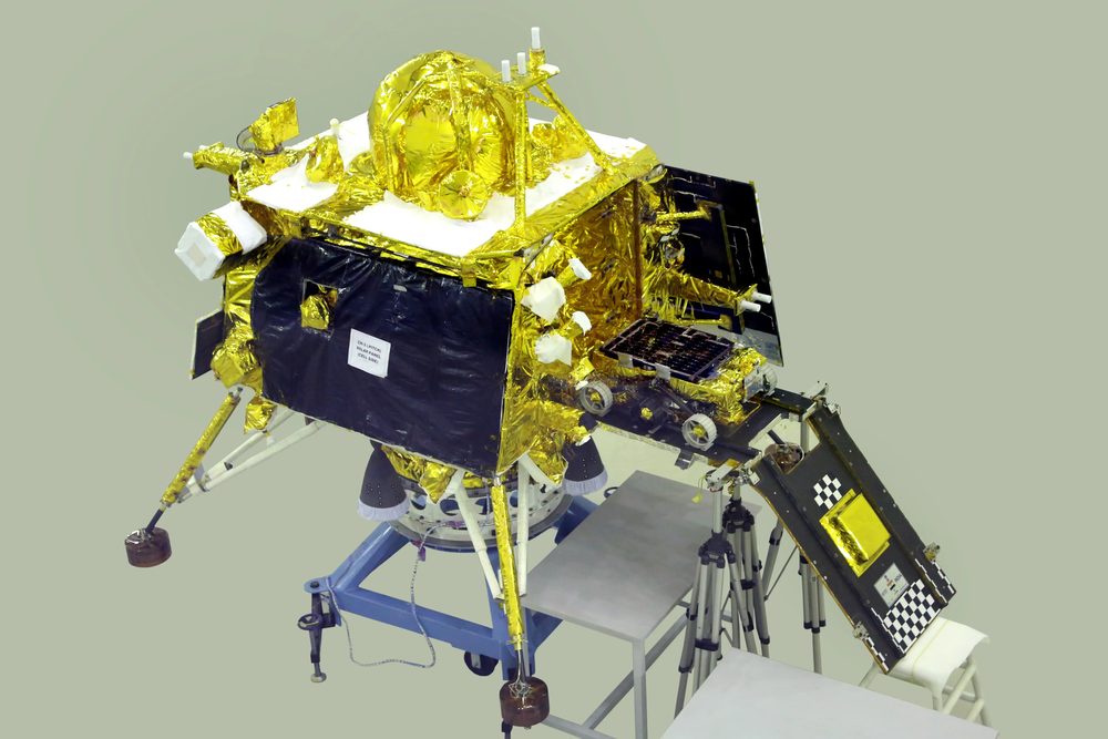 Gold-foiled four-legged lander on a stand, a chequered ramp lowered to one side