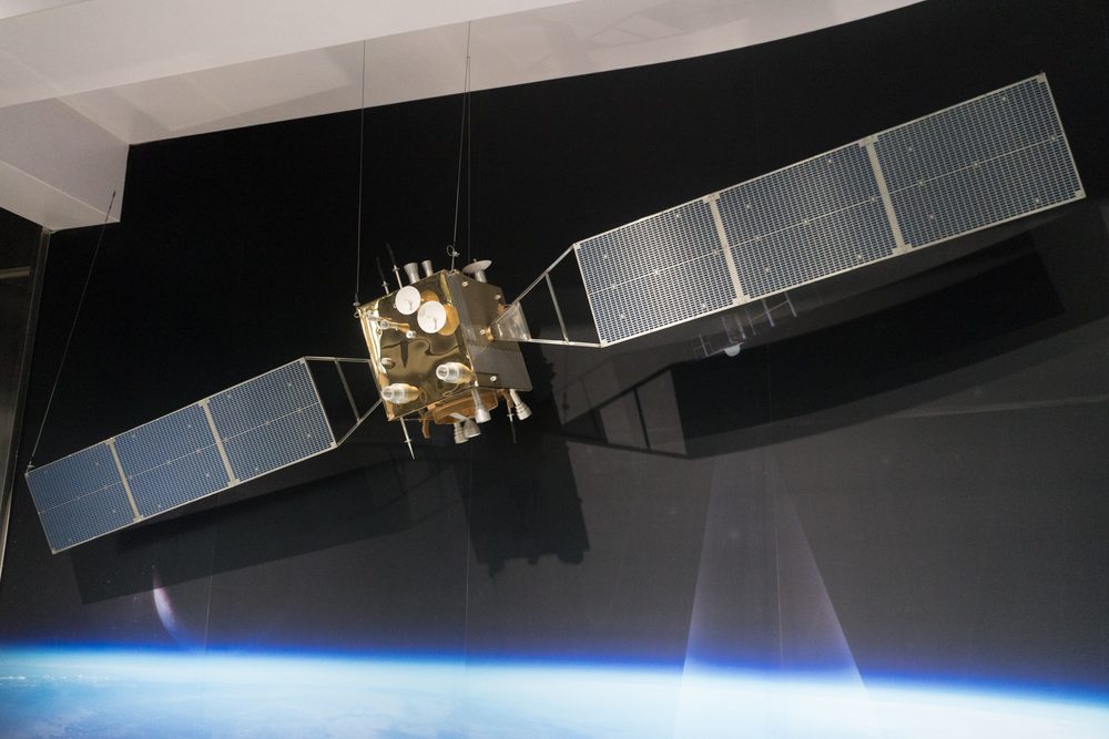 Gold-wrapped cubic satellite with two flat solar wings, hung before a painted Earth limb