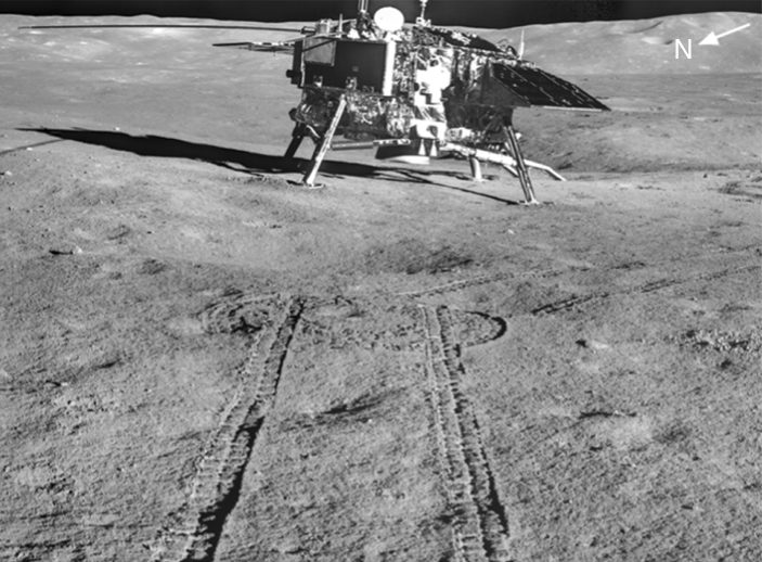 Four-legged lander on grey ground, twin wheel tracks curving towards the camera in foreground