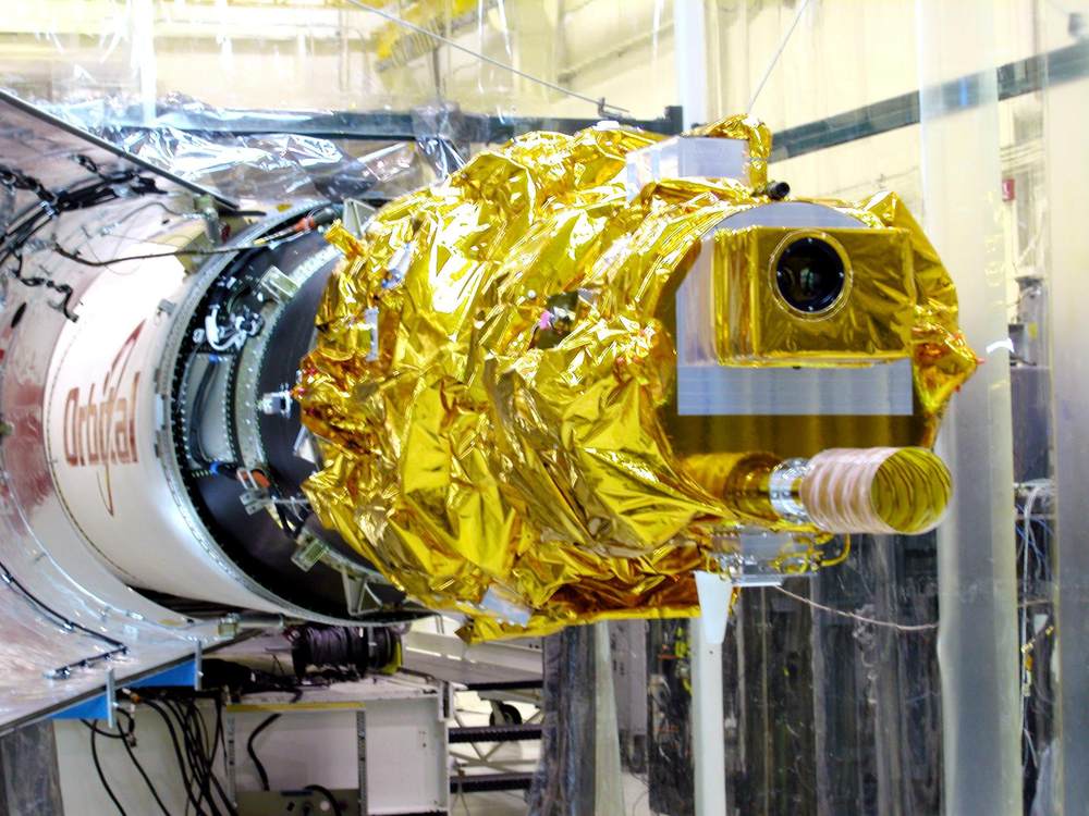 Gold-foil-wrapped spacecraft on its stage in a clean room, camera lens facing forward