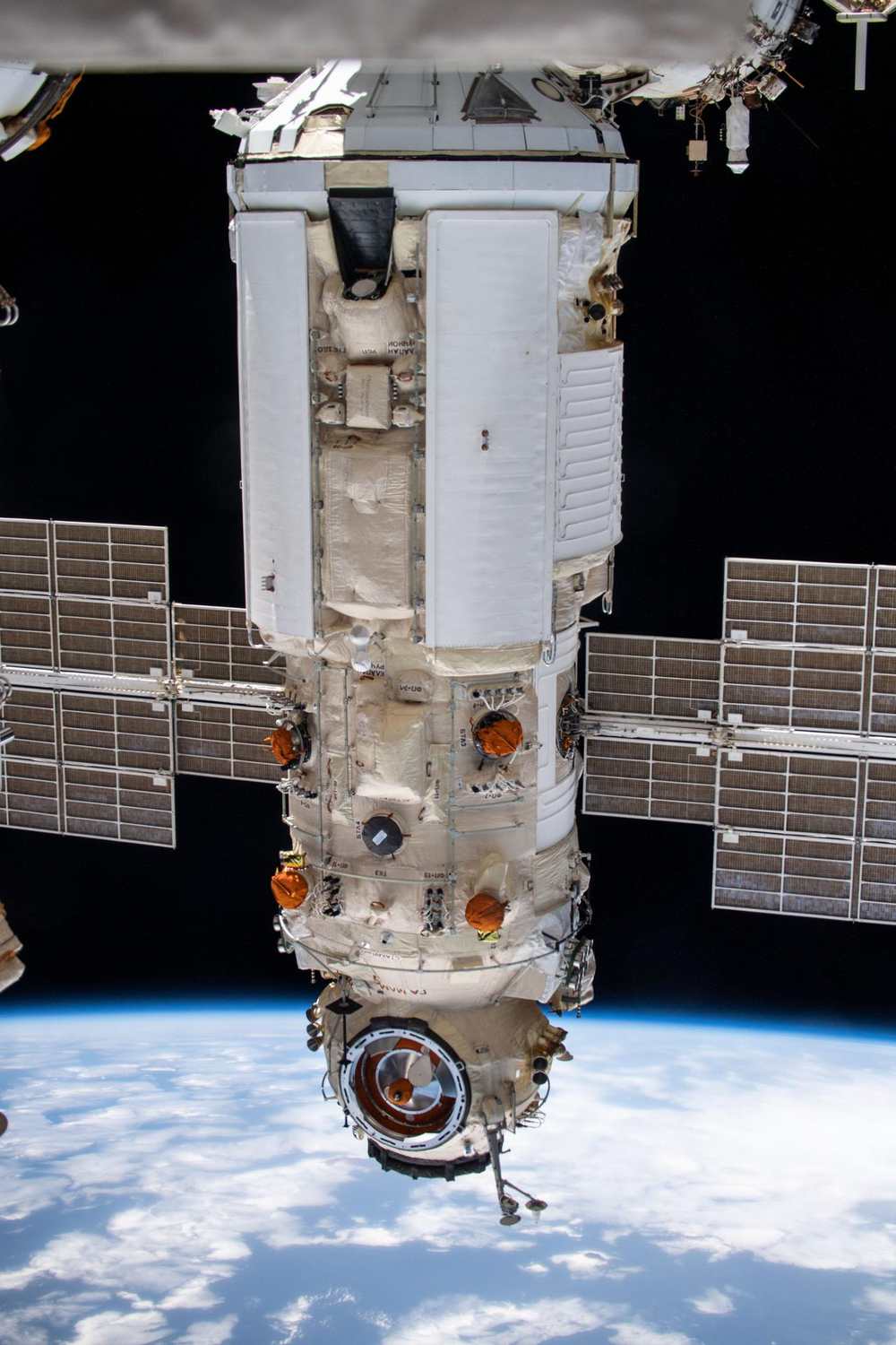 Long white module with two solar arrays hanging from the station above cloudy Earth