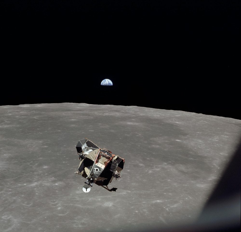 Angular silver and black vehicle low over a heavily cratered grey plain