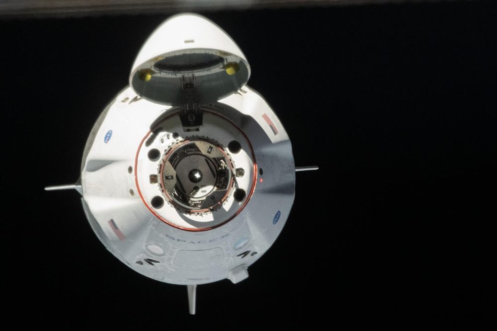 The capsule head-on and brightly lit against black, hinged nose cap folded back above
