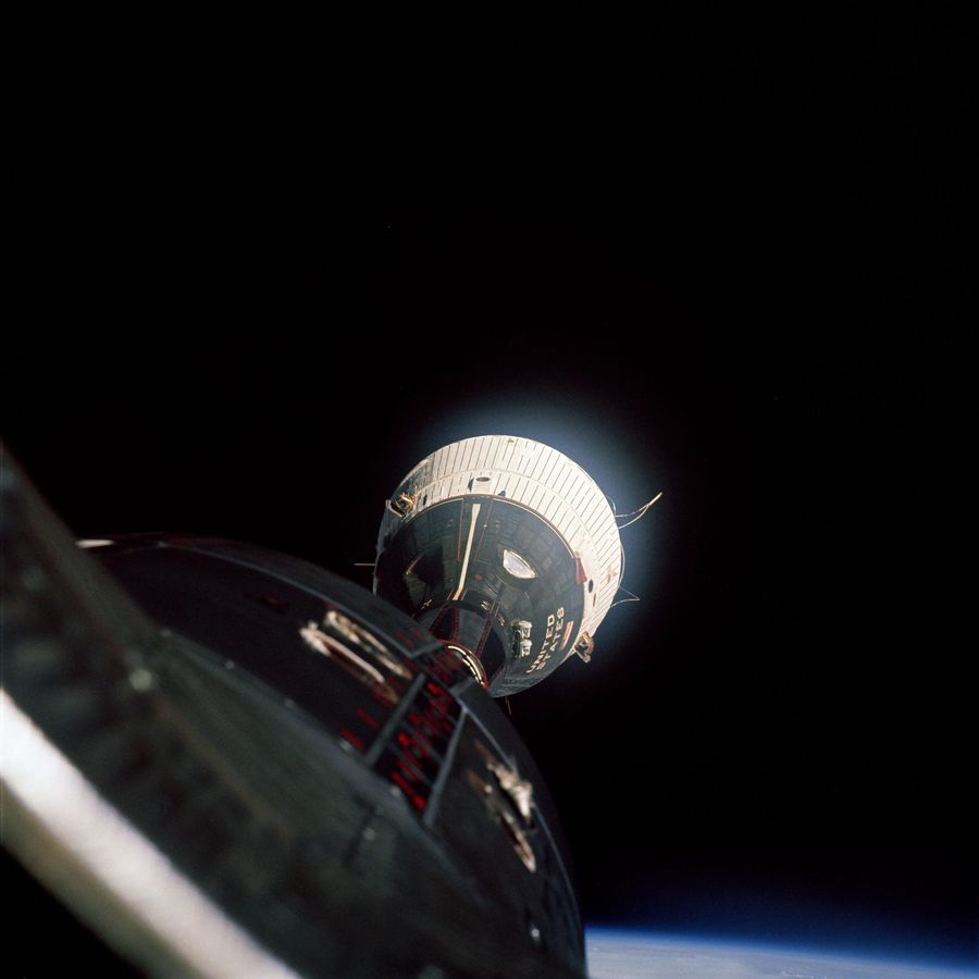 Distant capsule with a white shingled adapter section, the photographing spacecraft&rsquo;s nose in the foreground