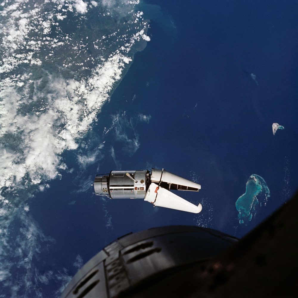 Bright target vehicle against deep blue ocean and scattered cays, seen past a dark hull