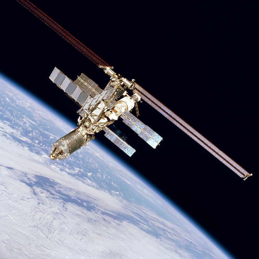 A part-built station with one long truss and a few array pairs above blue Earth