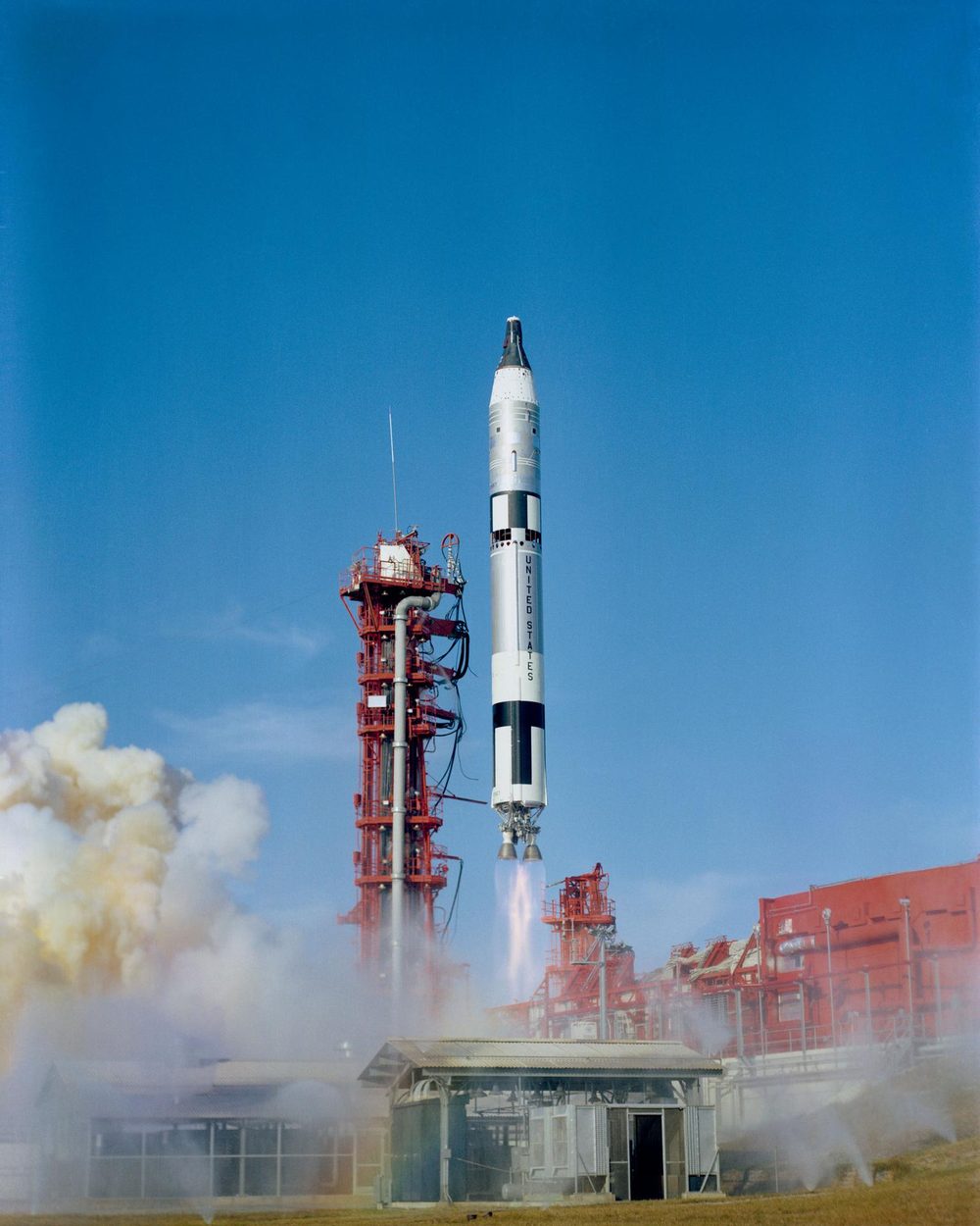 A slim white and black rocket climbs above its red gantry, twin engine plumes below